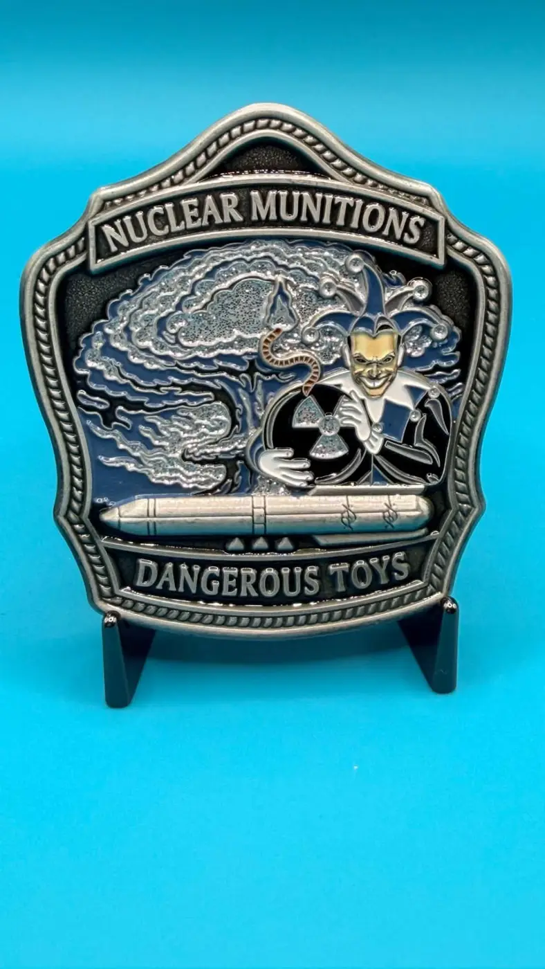 Front of the silver and blue Nuclear Munitions Dangerous Toys coin with a jester, blast, and missile