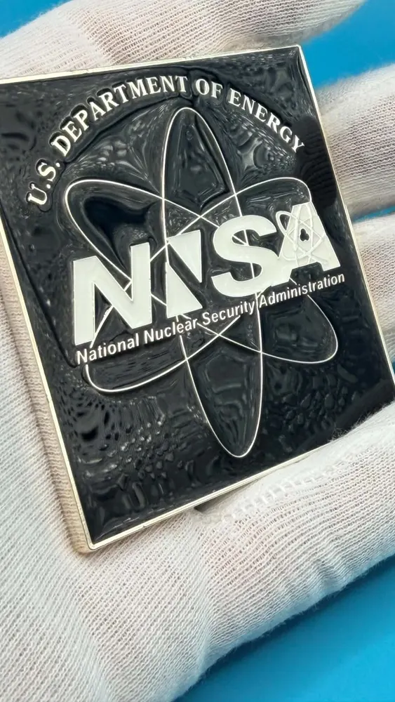 Front of the NNSA challenge coin with the National Nuclear Security Administration atom and wordmark in silver on black enamel
